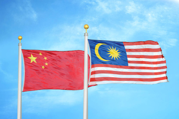 Κίνα και Μαλαισία δύο σημαίες σε κοντάρια σημαίας και μπλε θολό φόντο του ουρανού - Φωτογραφία, εικόνα