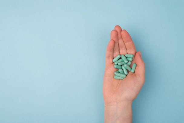 Top above overhead pov close up view photo of hands holding handful of pills isolated on blue background with blank copy empty space - Zdjęcie, obraz
