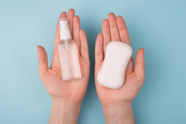 Pov top nad hlavou detailní pohled fotografie ženy, jak si vybírá mezi dvěma produkty, které drží na rukou mýdlo a průhledné antiseptické izolované přes modré pozadí - Fotografie, Obrázek