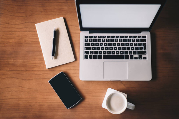Posto di lavoro in ufficio scrivania con computer portatile, una tazza di caffè, smartphone e notebook su scrivania in legno.
. - Foto, immagini