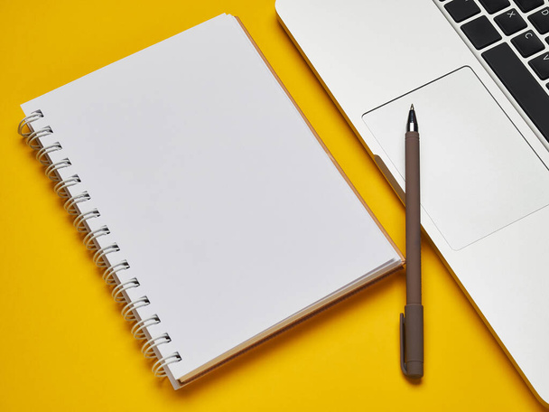 Workplace - laptop, notebook and pen for remote work on a yellow background table. Freelance desktop for home or office. Background with copy space. - 写真・画像