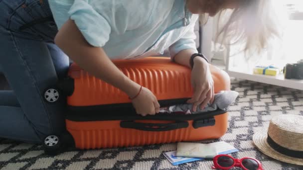 Jong meisje staat op elleboogson op overvolle oranje koffer, proberen om het te sluiten - Video