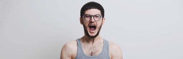 Panoramatický portrét mladého křičícího chlapa s kulatými brýlemi, izolovaný na bílém pozadí studia. - Fotografie, Obrázek