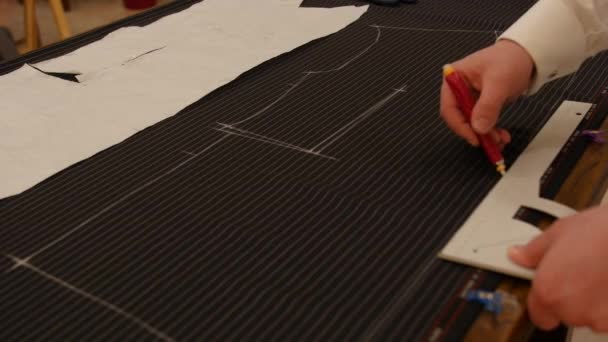 Krawiec w pracy, linia rysunkowa na czarnej tkaninie w paski z kredą. Projektant mody lub krawiec pracujący z tkaniną w studiu pełnym narzędzi krawieckich. Projektant tworzy szablon przyszłych ubrań. - Materiał filmowy, wideo