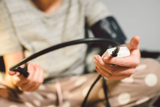 A téma a magas vérnyomás a magas vérnyomás betegség. Makró makró fiatal kaukázusi nő kezet automatikus tonométer segítségével ellenőrizze a nyomást otthon ágyon a hálószobában. - Fotó, kép