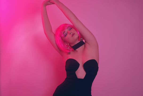 Look girls at the party. A girl in a black dress with a deep neckline and a pink square, short hair, dances, rejoices. Bright hair for the summer. The girl smartly moves to music, dancing, club, party.  - Foto, Imagen