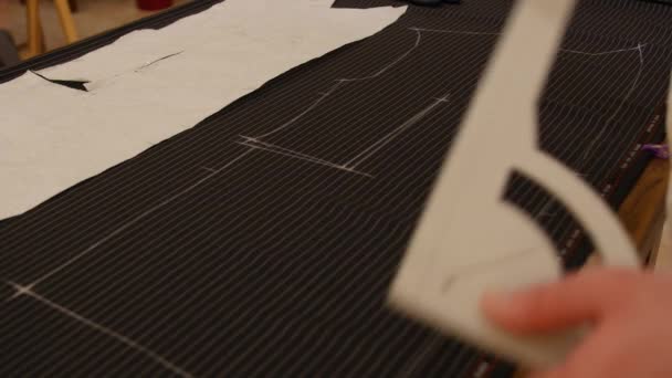 Tailler au travail, tracer une ligne sur tissu rayé noir avec de la craie. Créateur de mode ou tailleur travaillant avec du tissu dans le studio plein d'outils de couture. Designer crée un modèle de vêtements futurs
. - Séquence, vidéo