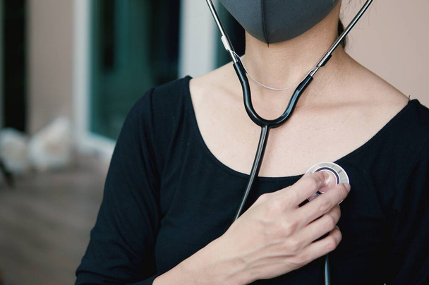 Hava kirliliği veya virüs salgınından korunmak için maske takan Asyalı bir kadın ve elinde stetoskop tutarken, Covid-19 durumundan endişe ediyordu.. - Fotoğraf, Görsel
