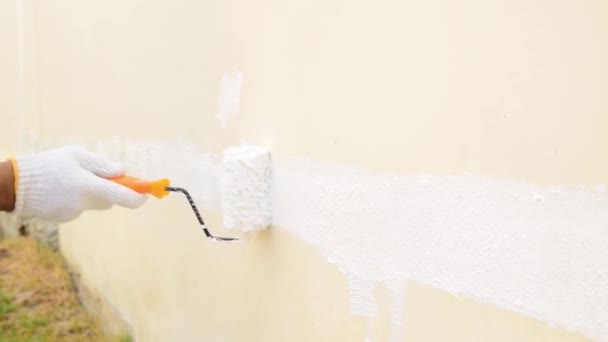 Close-up van een hand dragen van witte doek handschoenen, met behulp van een roller voor het schilderen van witte kleur op de betonnen muur. - Video