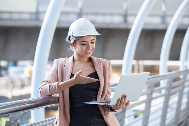 молодая красивая женщина инженер белая шляпа стоит, работая с ноутбуком
. - Фото, изображение