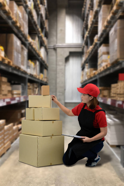 倉庫の背景には、女性スタッフや小包ボックスが在庫確認や発送準備のための商品をチェックし、ぼやけています - 写真・画像