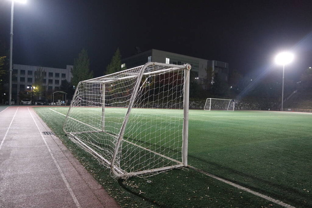 Vista nocturna de una red de portería de fútbol bajo luces de inundación. Vista de primer plano de la red de goles en un patio de fútbol - Foto, imagen