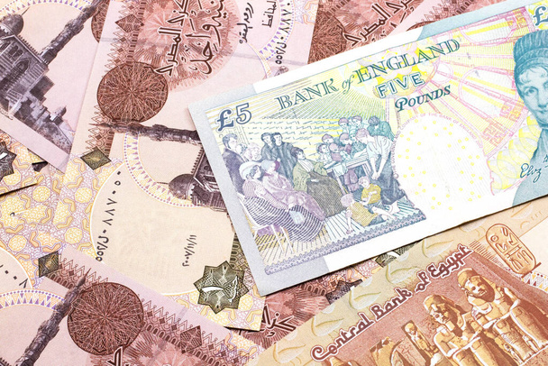 Μια κοντινή εικόνα ενός πολύχρωμου χαρτονιού πέντε λιρών από το Ηνωμένο Βασίλειο σε φόντο αιγυπτιακών χαρτονομισμάτων μιας λίρας σε μακροοικονομική - Φωτογραφία, εικόνα