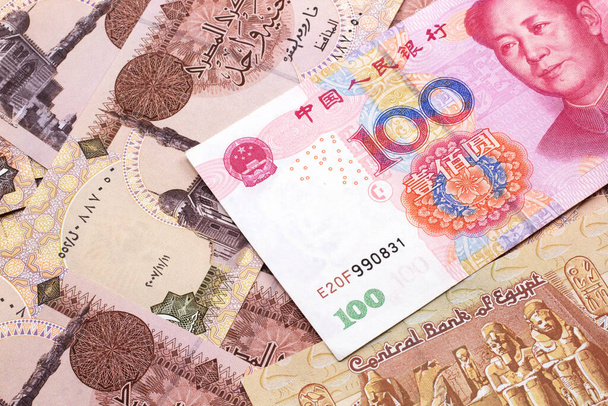 A close up image of a red, one hundred Chinese yuan bank note, close up on a background of Egyptian one pound bank notes.  Shot in macro - Photo, Image
