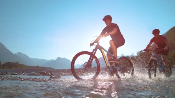 SUPER SLOW MOTION Jungs fahren E-Bikes entlang des flachen Flusses und planschen im Wasser - Filmmaterial, Video