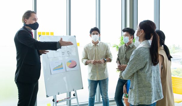 Small business startup multiracial Brainstorm meeting with chart paper board everyone mask for covid-19 protection coronavirus influenza megakadályozzák az egészséges ötletek koncepció iroda háttér. - Fotó, kép