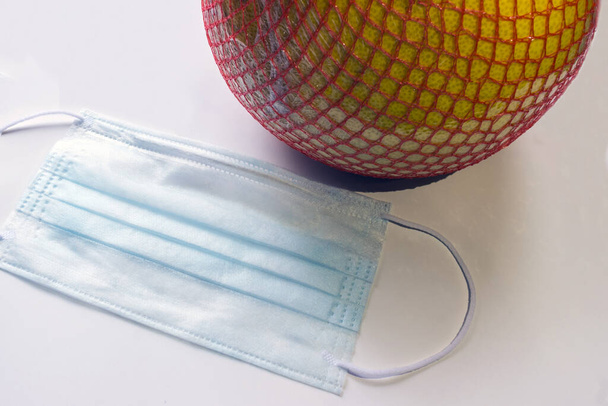 a disposable virus protection mask next to a fruit from the store. Risk of infection from contact with food. Wash your hands and do not touch things in the store. Treatment for coronovirus. - Photo, Image