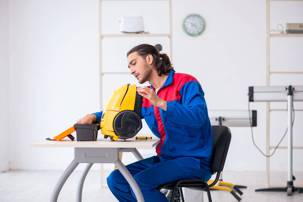 Jonge mannelijke aannemer repareert stofzuiger in werkplaats - Foto, afbeelding