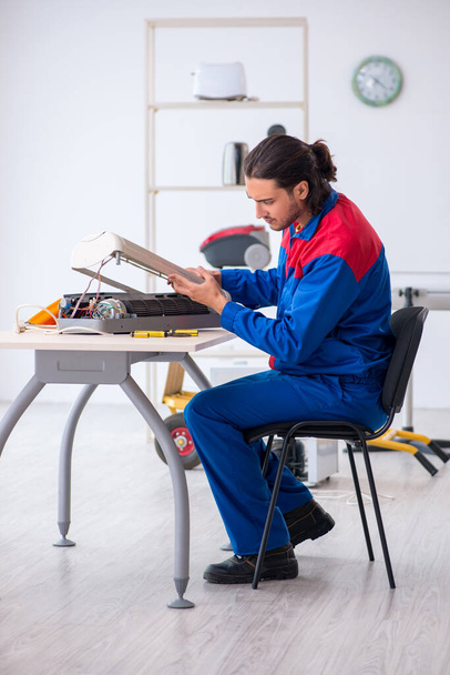 Jonge mannelijke aannemer repareert airconditioner in werkplaats - Foto, afbeelding