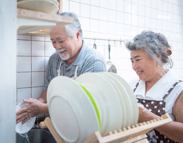 Happy asian elder senior couple washing dishes in sink at home in kitchen at home. - Photo, Image