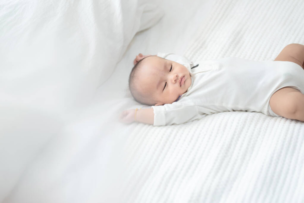 édes két hónapos újszülött fiú aludni fehér lepedőn ágy, ázsiai kis baba szunyókál az ágyban otthon. - Fotó, kép