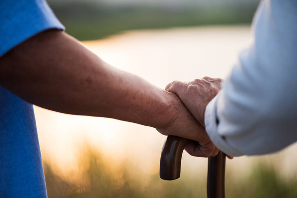 Onnellinen vanhempi pari aasialainen vanha mies ja nainen pitävät toisiaan kädestä ja seisovat kesällä lähellä vuorta ja järveä auringonnousun tai auringonlaskun aikana. Vanhempi terveydenhuolto ja parisuhteen käsite
. - Valokuva, kuva