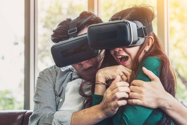 自宅のリビングルームで仮想現実VRヘッドセットでビデオを見て幸せなカップル。マルチメディア映画とエンターテイメントのコンセプト. - 写真・画像