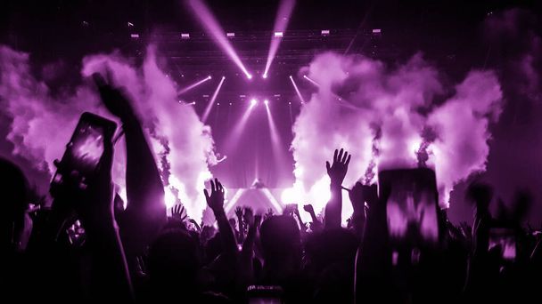 Onnelliset ihmiset tanssivat yökerhon DJ-keikalla ja kuuntelevat DJ:n elektronista tanssimusiikkia lavalla. Siluetti iloinen väkijoukko juhlia uudenvuoden puolue 2020. Ihmiset elämäntapa DJ yöelämä. - Valokuva, kuva