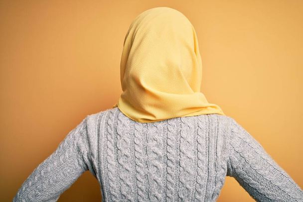 Jeune belle fille afro-américaine portant hijab musulman sur fond jaune isolé debout vers l'arrière regardant loin avec les bras sur le corps
 - Photo, image