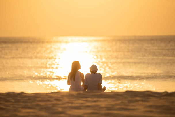 Pár zamilovaných při sledování západu slunce na letních prázdninách na pláži. Lidé silueta zezadu sedí těší pohled západ slunce moře na tropické destinace dovolenou. Romantický pár na pláži. - Fotografie, Obrázek