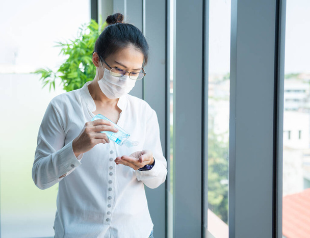Азиатская бизнес-женщина выжать алкоголь гель под рукой с масками износа предотвратить PM 2.5 в офисе, предотвратить микробов защиты от коронавируса или Covid-19 вируса мира пандемии, здравоохранения и медицины концепции
 - Фото, изображение