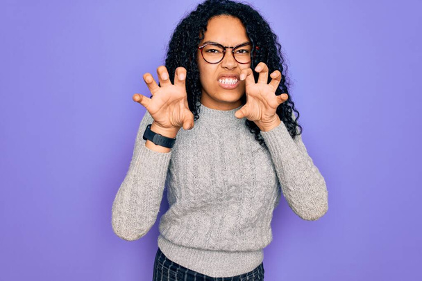 Young african american woman wearing casual sweater and glasses over purple background smiling funny doing claw gesture as cat, aggressive and sexy expression - Photo, Image