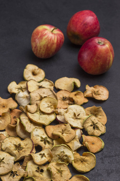 Three fresh red apples and slices of dried apples on black background. Diet vegetarian food - Foto, Imagen