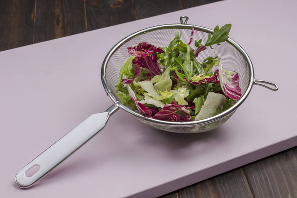 Multicolored leafy vegetable mix in metal colander. Vegan food. Clean eating. Pink background - Фото, зображення