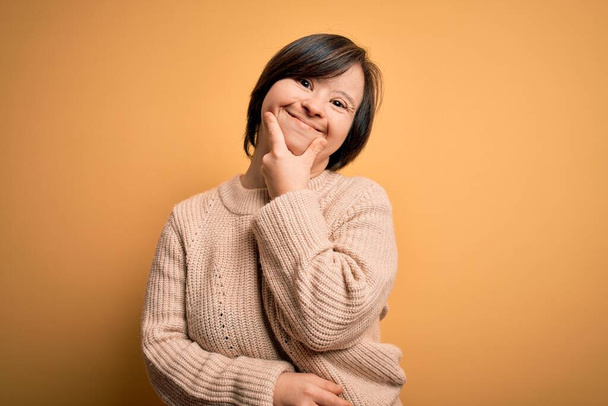 Young down syndrome woman wearing casual sweater over yellow background looking confident at the camera smiling with crossed arms and hand raised on chin. Thinking positive. - Photo, Image