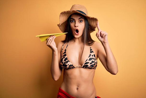 Nuori kaunis nainen lomalla yllään bikinit ja kesän hattu tilalla paperi lentokone yllättynyt idea tai kysymys sormella onnellinen kasvot, numero yksi
 - Valokuva, kuva