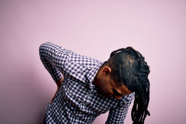 Junger gut aussehender afro-amerikanischer Afro-Mann mit Dreadlocks trägt lässiges Hemd Leiden an Rückenschmerzen, Berührung mit der Hand, Muskelschmerzen - Foto, Bild