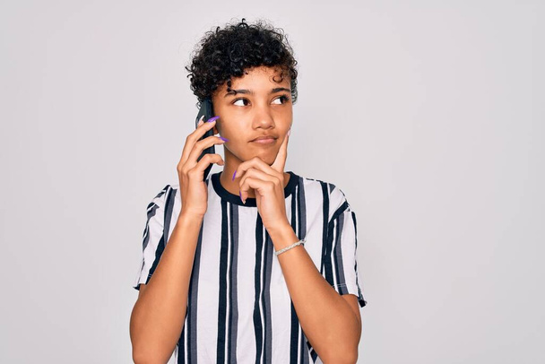 Young beautiful african american afro woman having conversation talking on the smartphone serious face thinking about question, very confused idea - Foto, Imagen