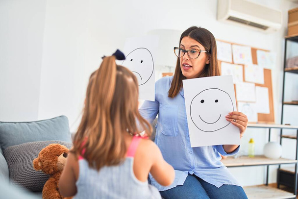 Młoda terapeutka mówiąca i lecząca dzieci, wychowawczyni i korygująca zachowanie w pokoju płac pedagogicznych z radosnymi i smutnymi twarzami - Zdjęcie, obraz