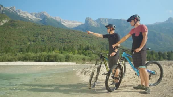 SLOW MOTION: Νεαροί ποδηλάτες ξεκουράζονται δίπλα στο ποτάμι και παρατηρούν όμορφα βουνά - Πλάνα, βίντεο