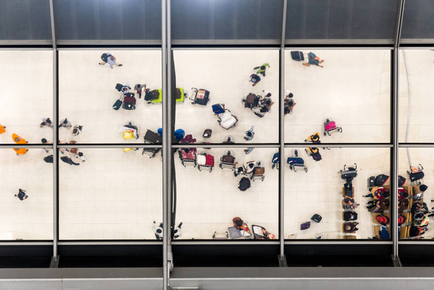 Havaalanında seyahat etmek için bavul ve evrak çantasıyla kuyrukta bekleyenlerin yansıma camı. - Fotoğraf, Görsel