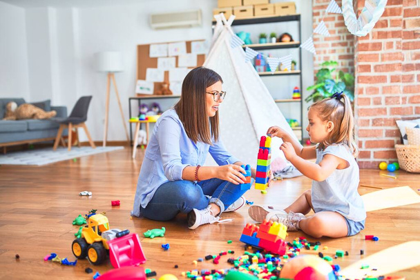 Caucasian girl kid playing and learning at playschool with female teacher. Mother and daughter at playroom around toys playing with bulding blocks - Foto, imagen