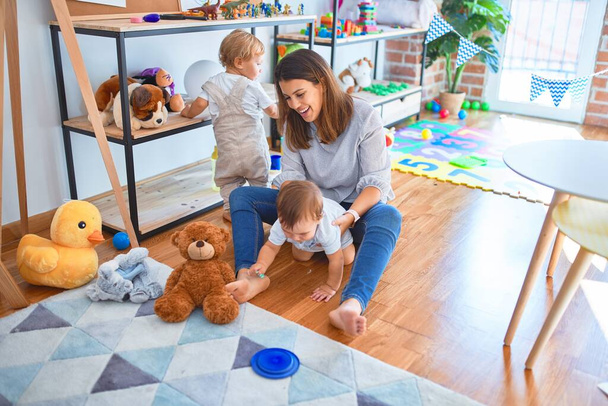 Beautiful teacher and toddlers playing around lots of toys at kindergarten - Photo, Image