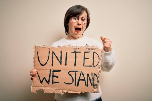 Молодая синдром Дауна женщина держит знак протеста с единым мы стоим права сообщение гордо кричать и праздновать победу и успех очень взволнован, аплодируя эмоции
 - Фото, изображение