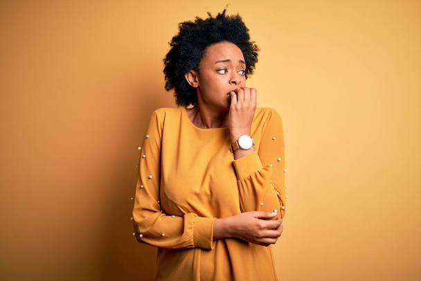 若い美しいアフリカ系アメリカ人のアフロ女性は、口の爪をかむ上で手でストレスと緊張を見てカジュアルなTシャツを着て巻き毛。不安の問題. - 写真・画像