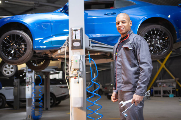 Cheerful handsome African male mechanic smiling to the camera confidently, working at car service - Photo, Image