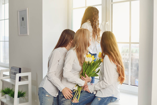 Hyvää äitienpäivää. Äiti ja kolme tytärtä kukkia katselee ikkunasta talossa
. - Valokuva, kuva