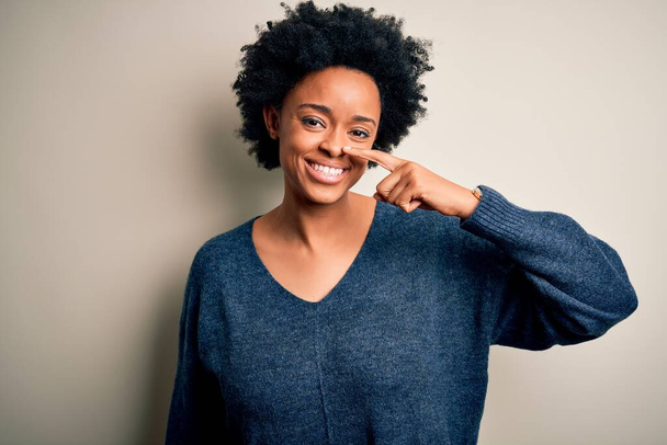 Young beautiful African American afro woman with curly hair wearing casual sweater Pointing with hand finger to face and nose, smiling cheerful. Beauty concept - Fotó, kép