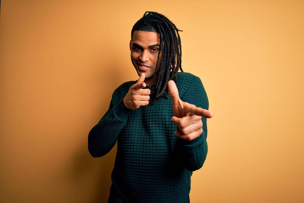 Jonge knappe Afrikaans-Amerikaanse afro man met dreadlocks met groene casual trui wijzende vingers naar camera met vrolijk en grappig gezicht. Goede energie en vibraties. - Foto, afbeelding