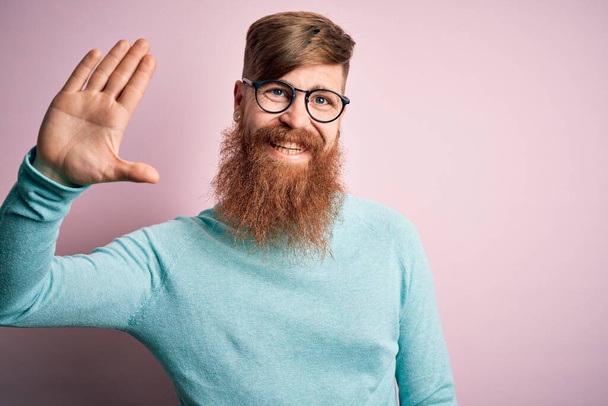 Красивый ирландский рыжеволосый мужчина с бородой в очках на розовом изолированном фоне, отказываясь сказать привет счастливый и улыбающийся, дружелюбный жест приветствия
 - Фото, изображение